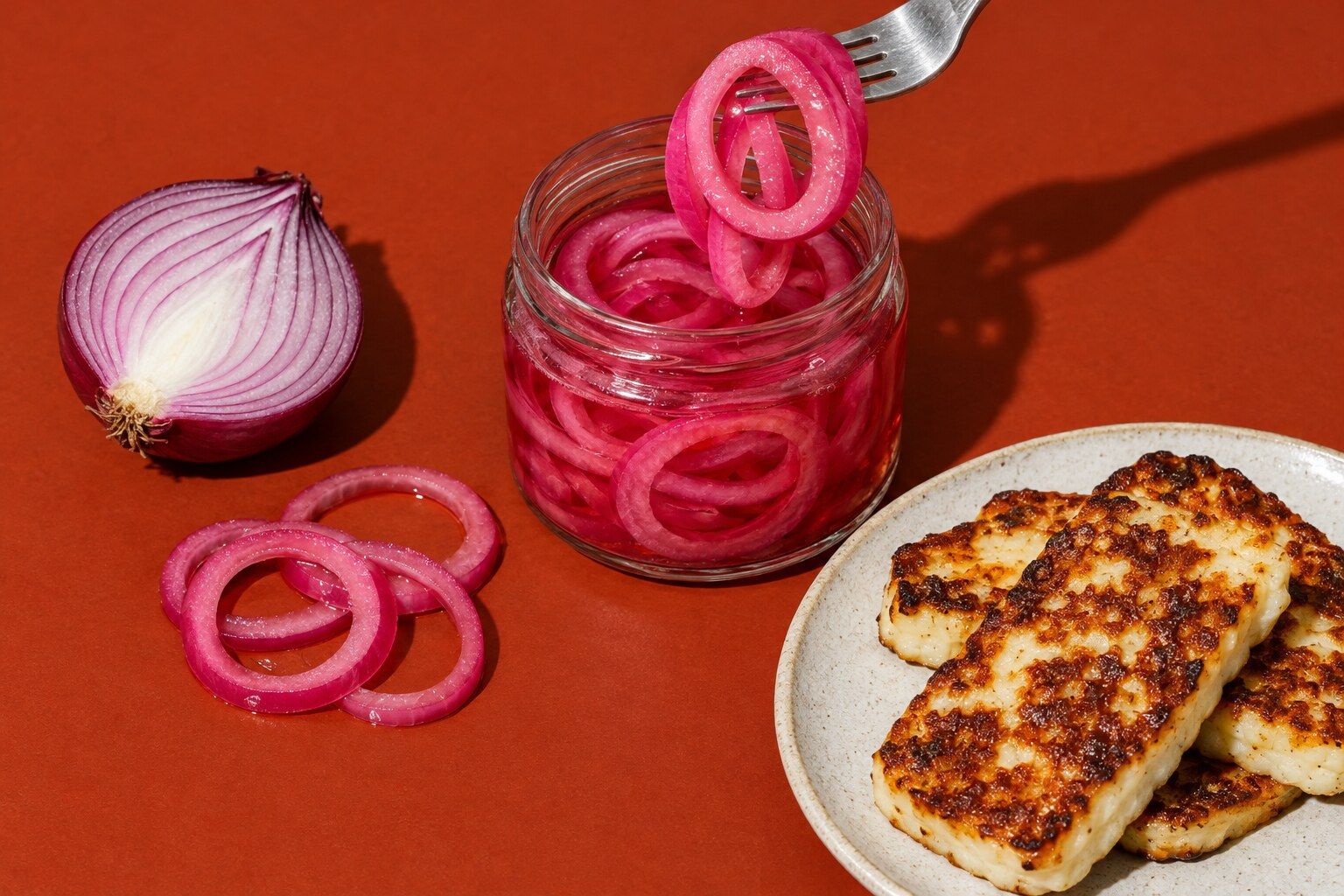 En glasburk med rosa picklade rödlöksringar och en gaffel som lyfter några av dem.